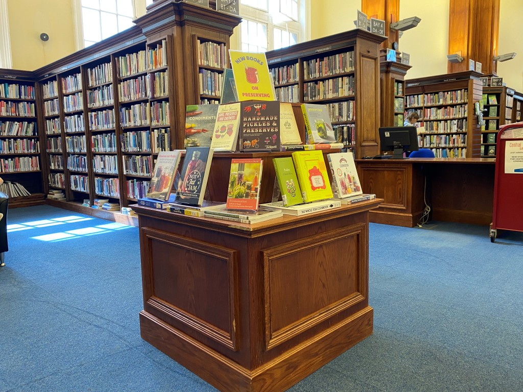A book display on top of a wooden cube unit in front of bays of bookshelves.