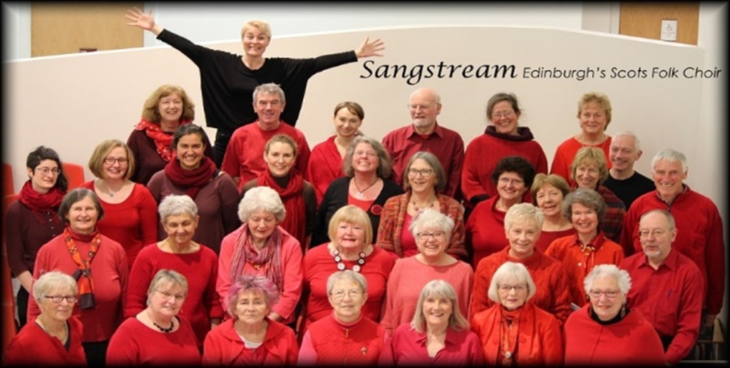 A choir of women and men wear red and pose for a group photograph.