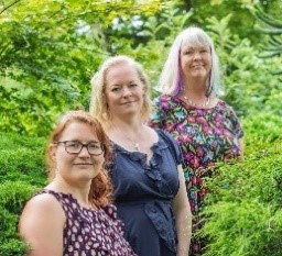 A portrait of three women taken surrounded by foliage. 
