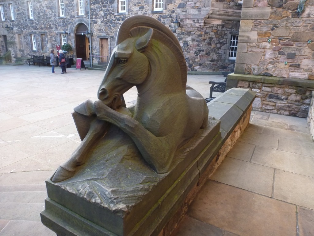 Stone statue of a lying unicorn on the edge of a paved courtyard.