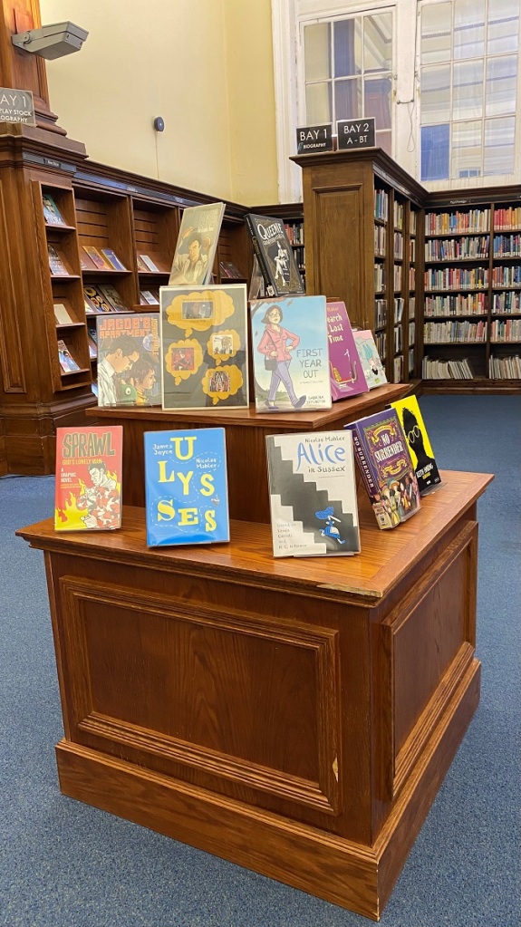 A display of graphic novels on a wooden plinth.