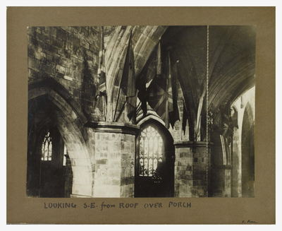 A black and white photograph of a church interior showing flags hanging from stone archways and tracery windows beyond.