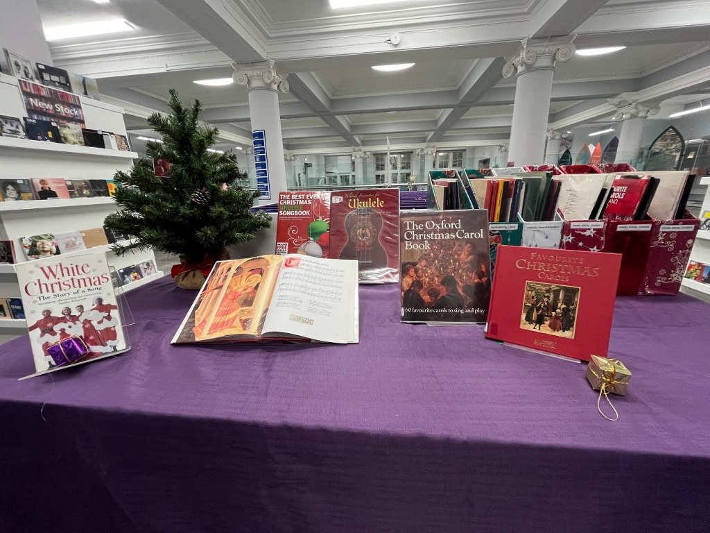 A display of Christmas songbooks, box files of sheet music and a mini Christmas tree on a table in a library.