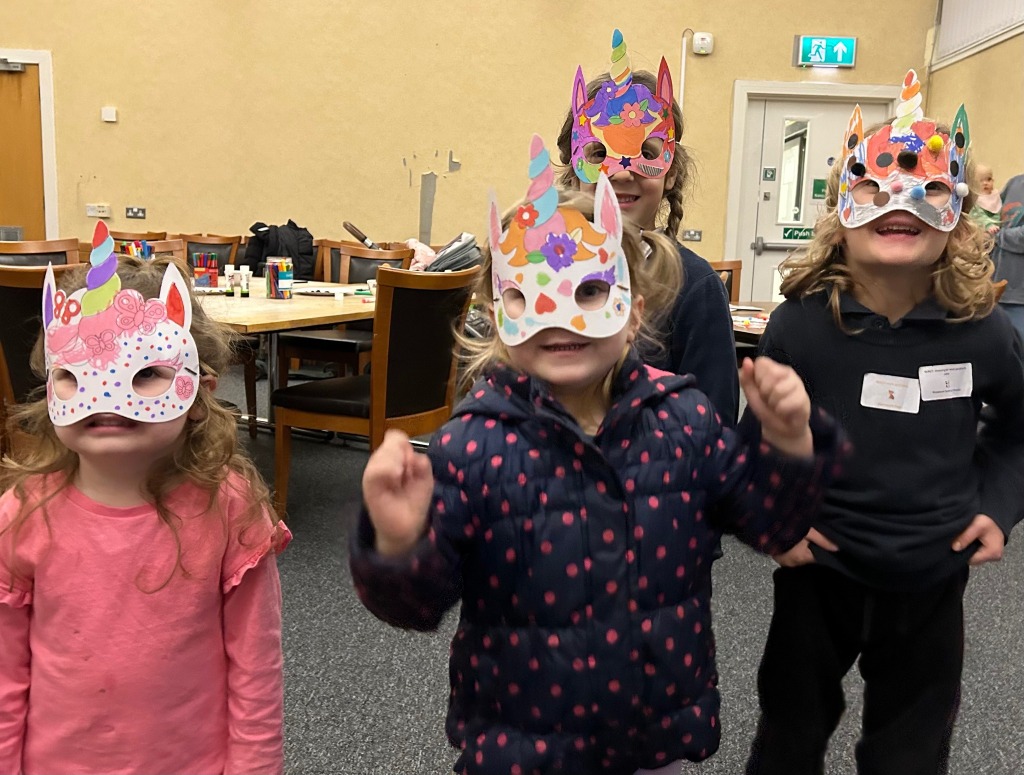 Four children photographed wearing decorated unicorn masks.