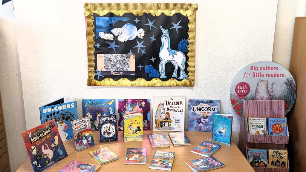 Unicorn themed children's books are displayed on a table beneath a picture of a unicorn in a gold frame.
