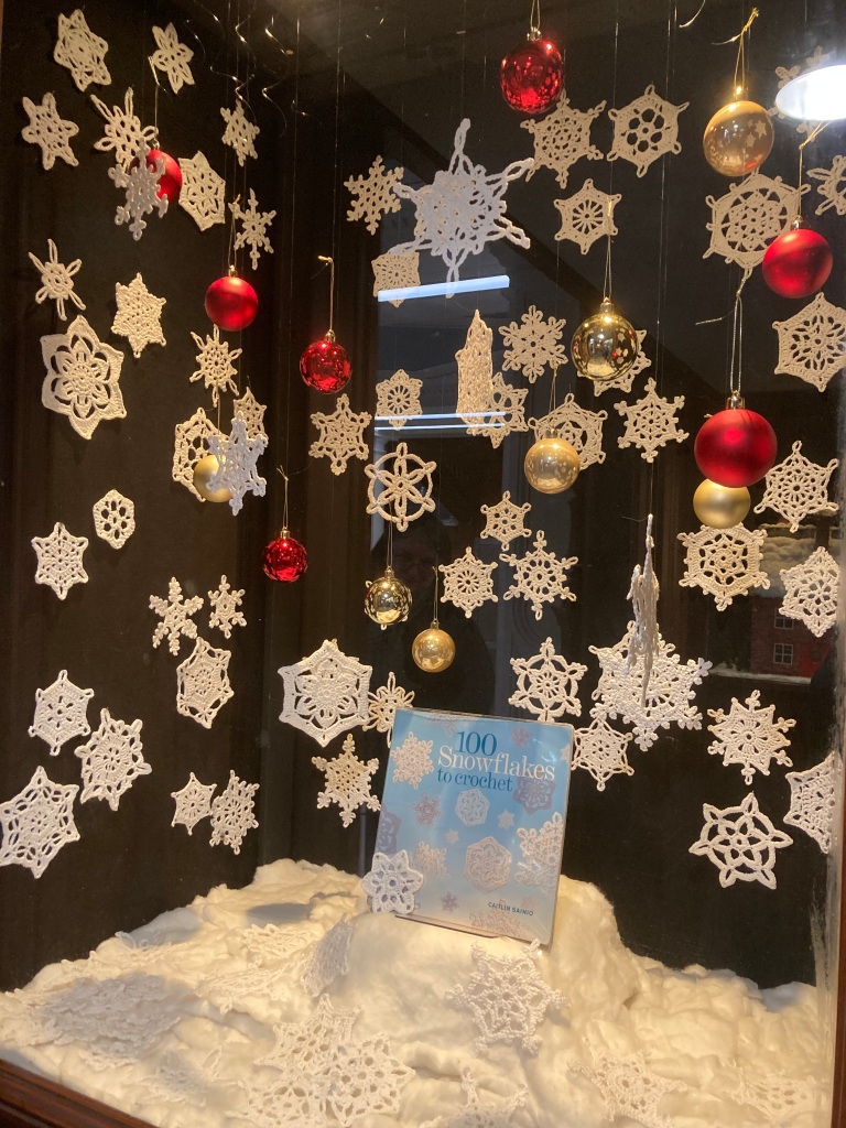 A display of hanging crocheted snowflakes surrounding a book entitled 100 Snowflakes to crochet. 