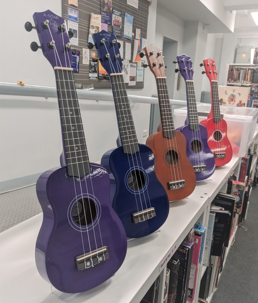A row of differently coloured guitars are displayed on top of book shelves.