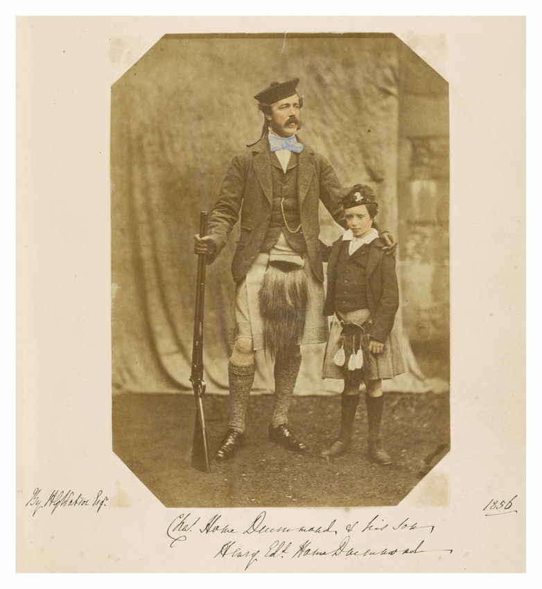 A man holding a rifle stands with his arm around the shoulders of young boy. Both are wearing kilts, sporrans and caps. 