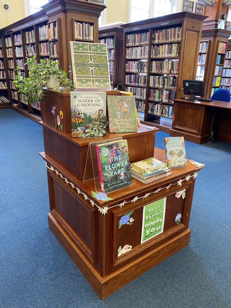 Gardening books are displayed alongside a pot plant on a wooden display stand.